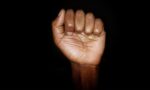 Fotografia de uma mão de pele negra fechada em punho em um fundo preto